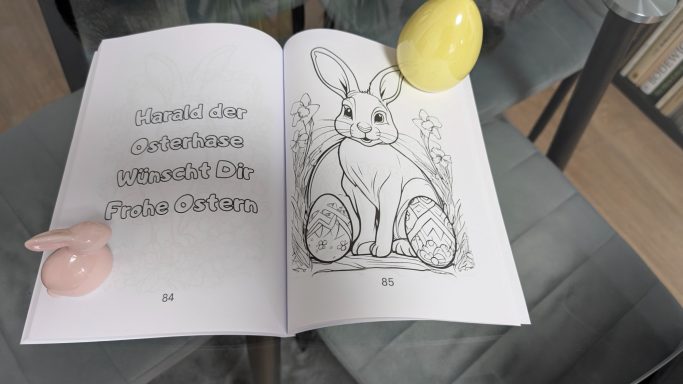 Offenes Malbuch mit einem Hasen, umgeben von einem rosa und einem gelben Ei.