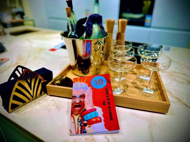 Ein Tisch mit Gläsern, einem Weinkühler, einer Flasche und einem Kochbuch.